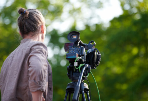 Rear view to man videographer recording outdoor movie about nature on professional camera, TV crew